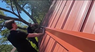 Installer fitting snow brakes along the edge of a red steel roof