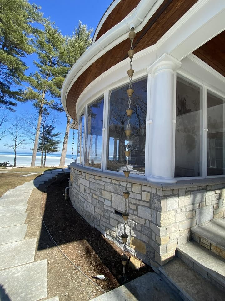 A copper rain chain hanging from a white half-round gutter on a lakefront home