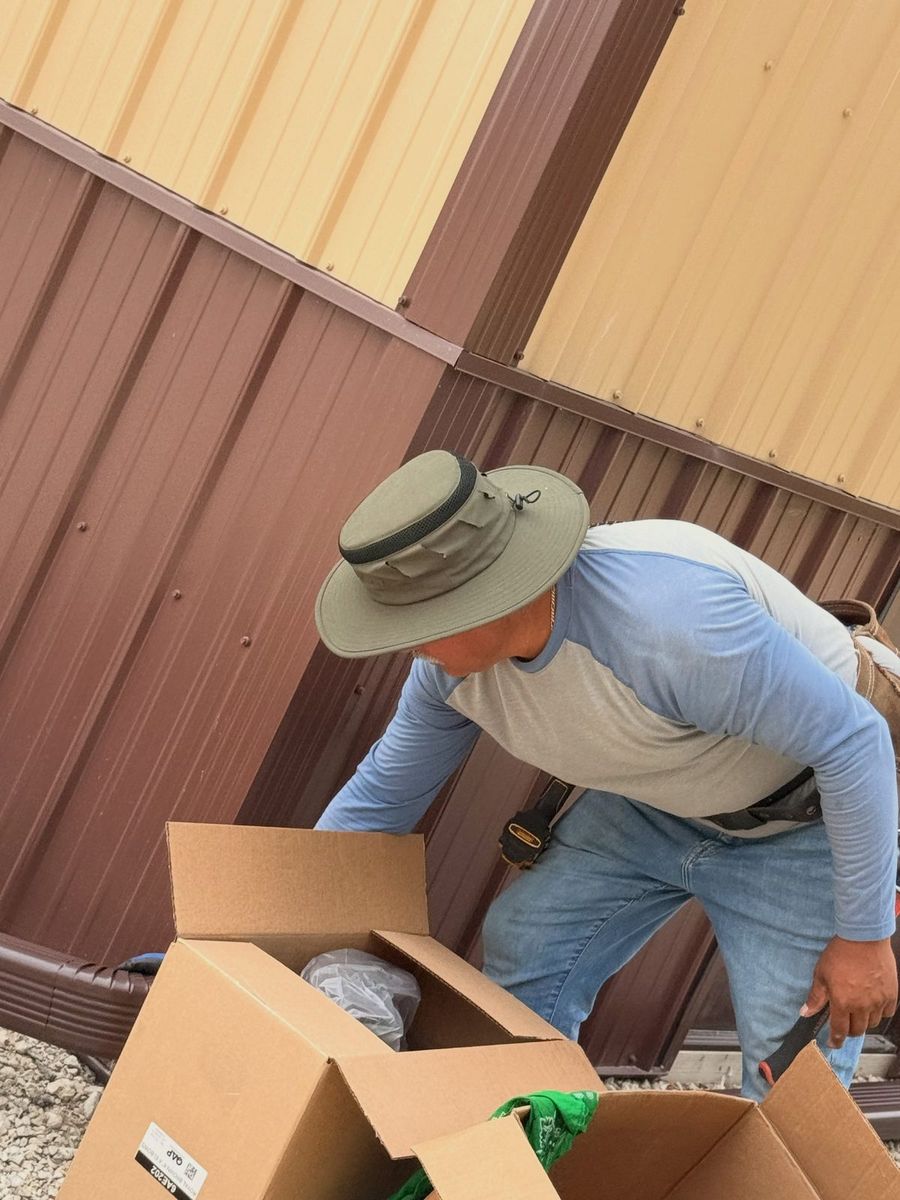 A crew member opening boxes of material beside a brown and tan steel pole barn